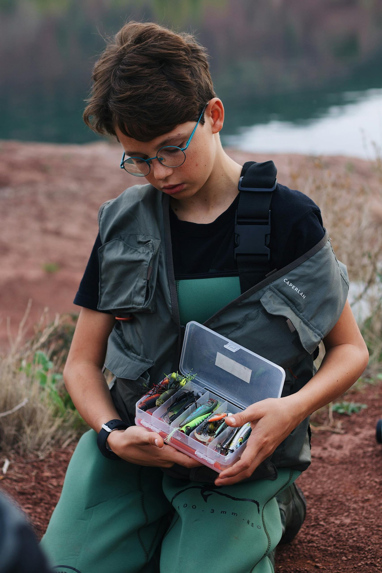 A young boy preparing his fishing gear by a tranquil lakeside in summer.