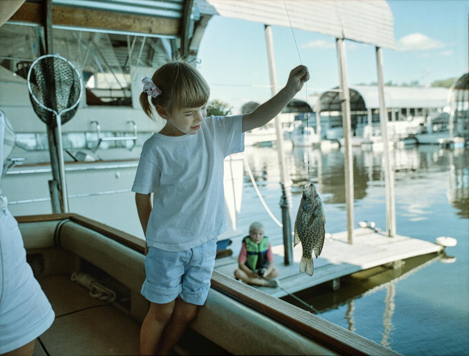 A child joyfully displays her catch at the marina on a sunny summer day.