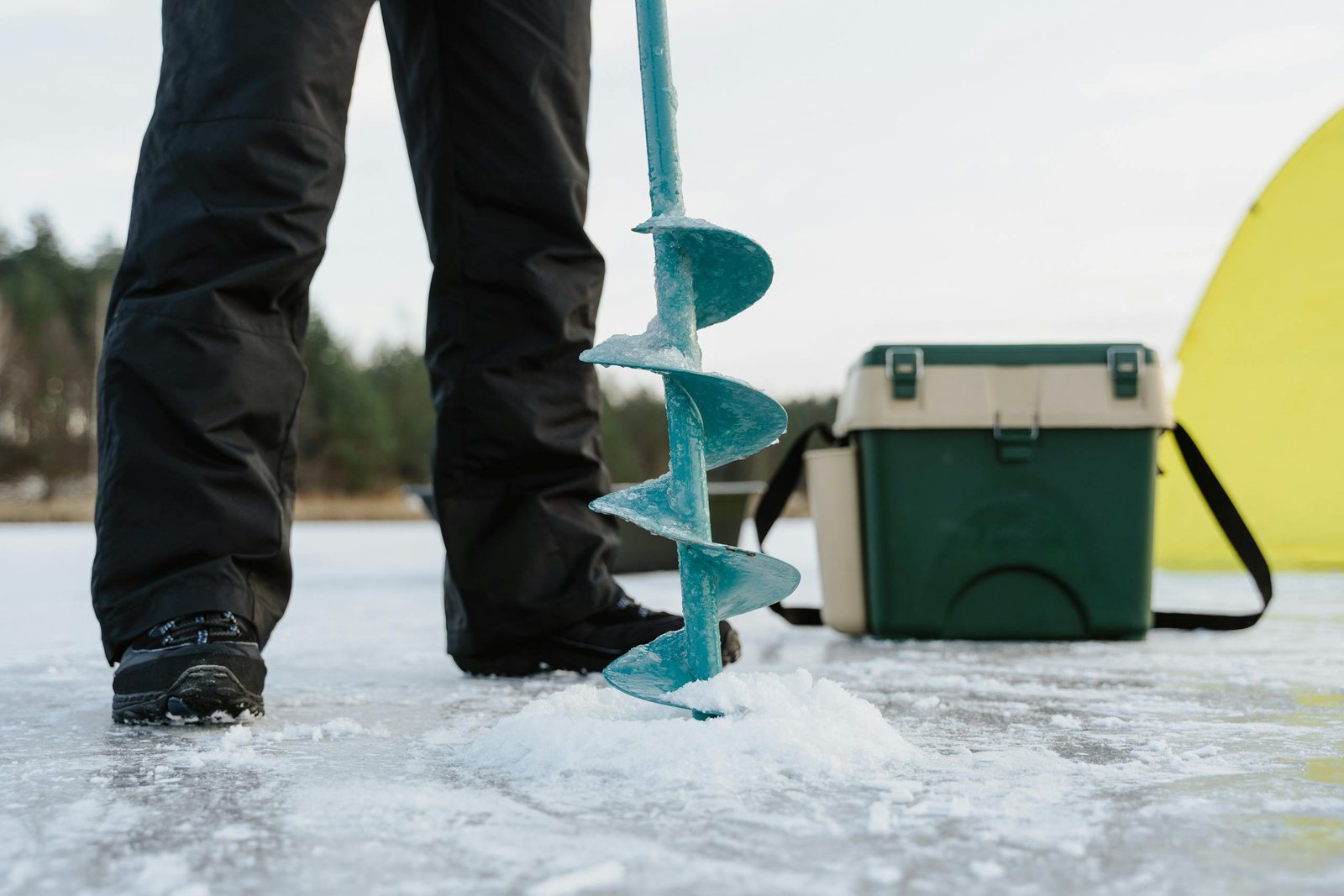A person preparing for ice fishing with an auger and gear on a frozen lake.