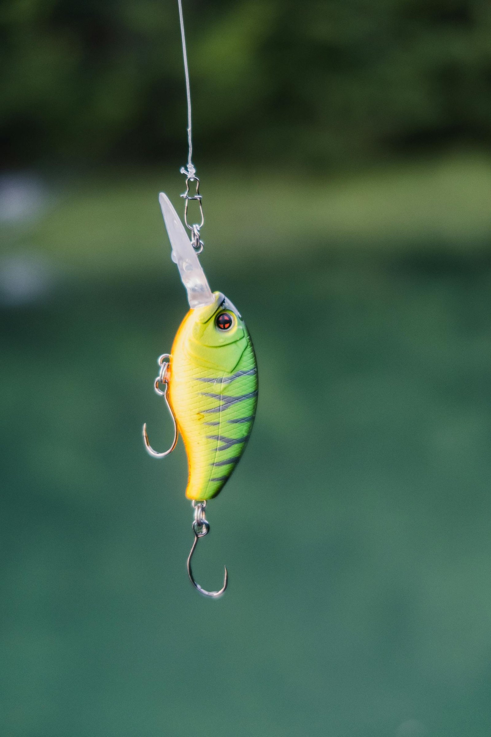 Close-up of a colorful fishing lure suspended above tranquil green waters.