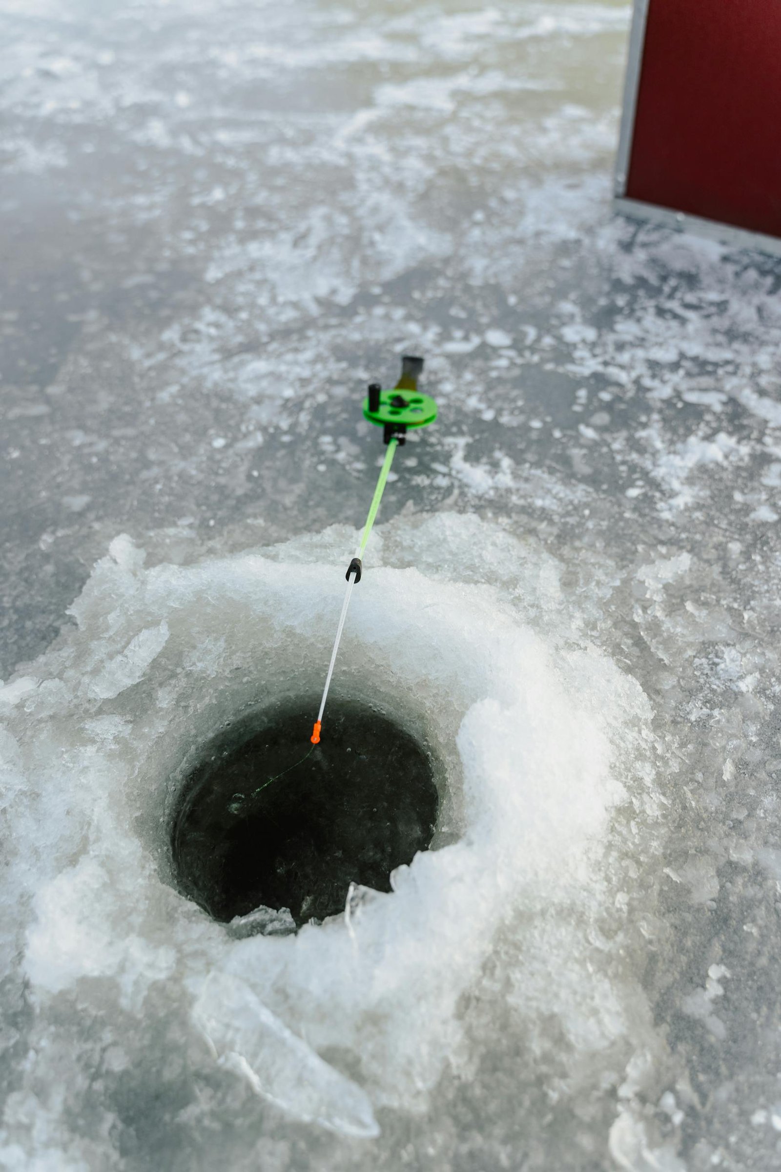 Close-up of an ice fishing hole with a fishing rod on a frozen lake surface.