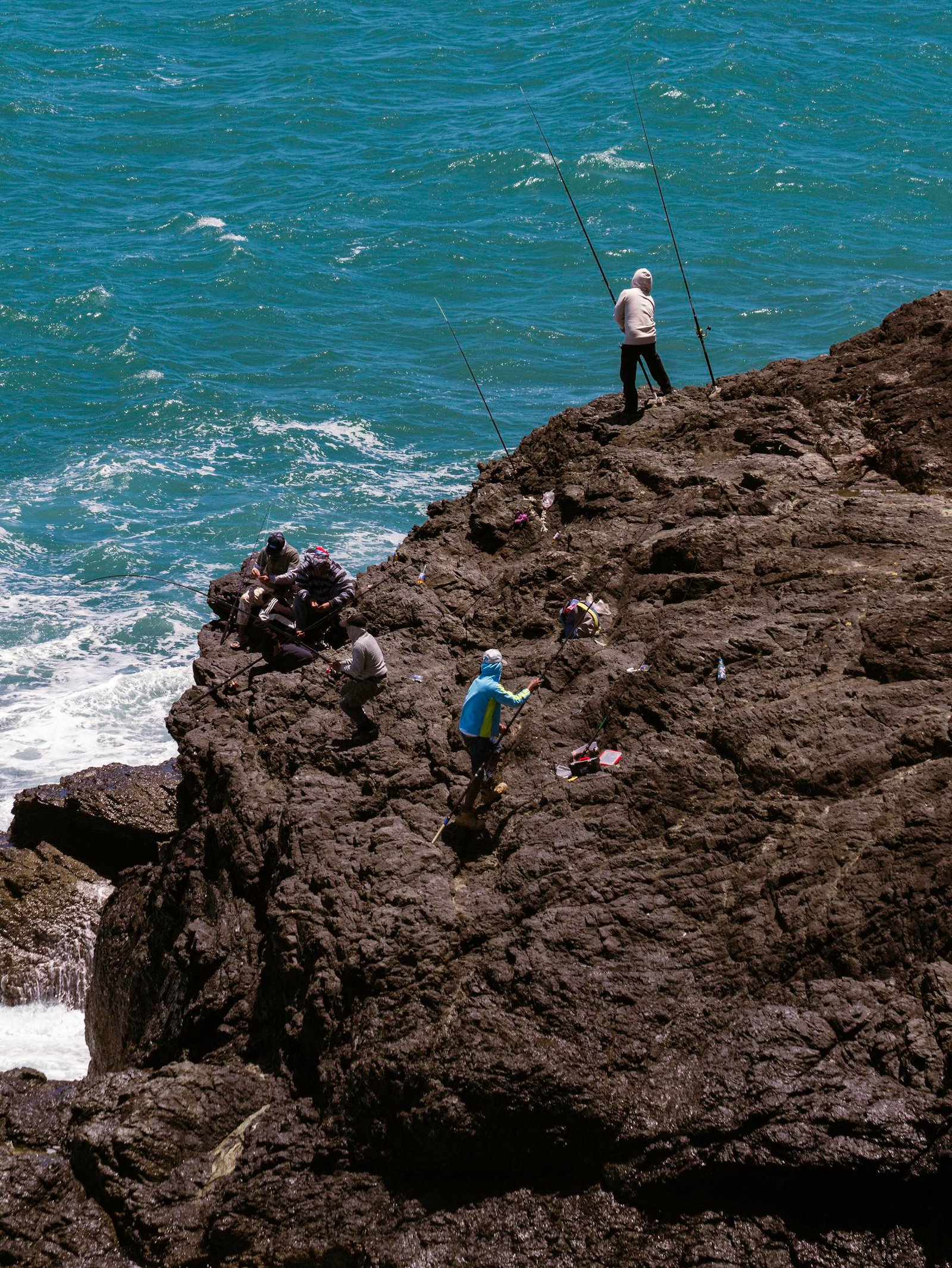 Fishermen casting lines from rocky coast with turquoise sea backdrop. Perfect for nature and adventure themes.