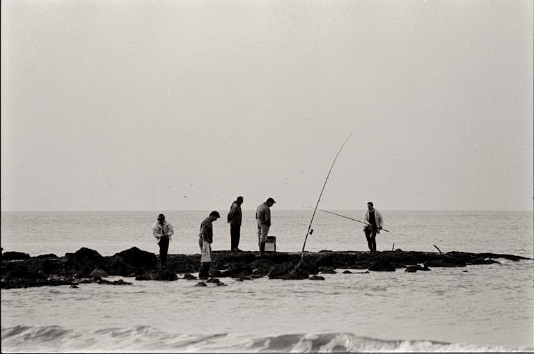 Best Fishing Spots in the US. Group of men fishing on the rocky shore in a black and white coastal scene.